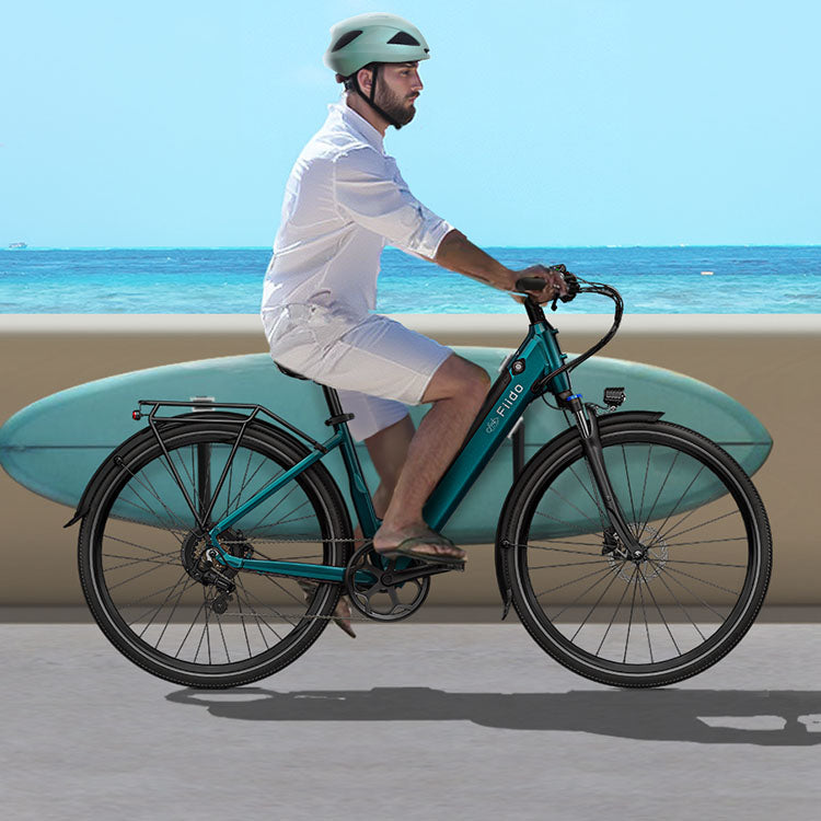 A man wearing a helmet rides a Fiido C11 electric bike while holding a surfboard.